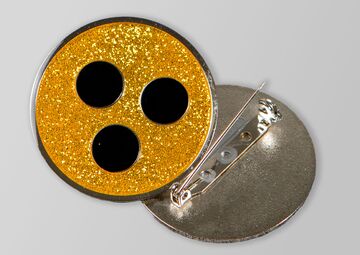 Ansicht auf eine gelbe Plakette mit drei schwarzen Punkten und Anstecknadel
