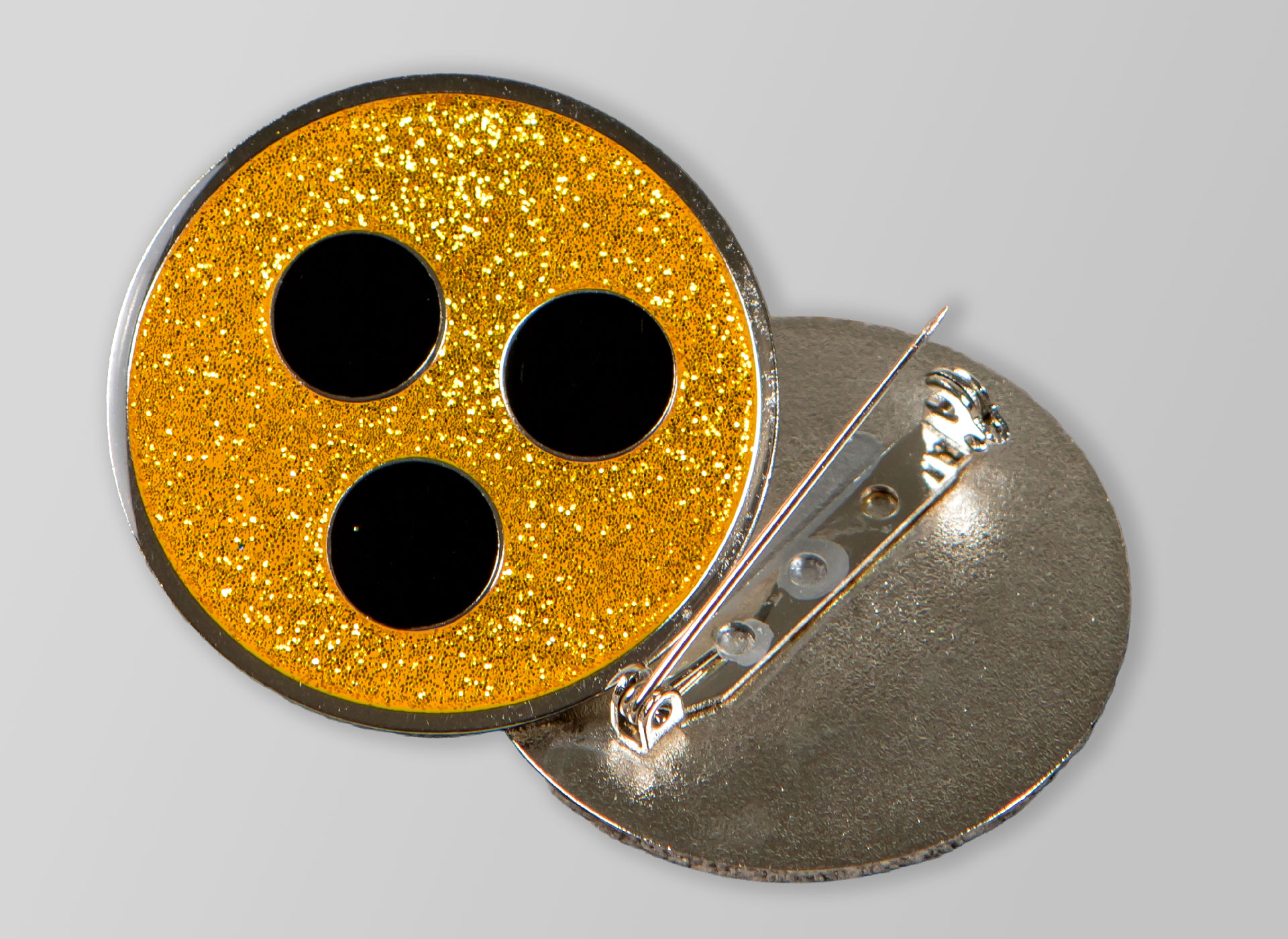 Ansicht auf eine gelbe Plakette mit drei schwarzen Punkten und Anstecknadel